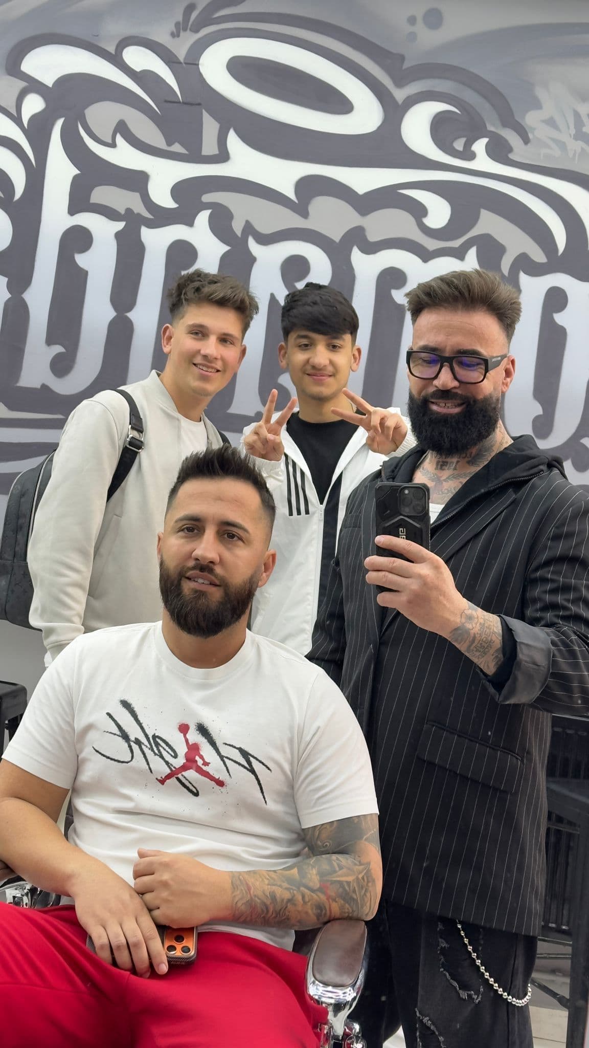 Grup de frizeri și clienți în fața muralului El Comandante — atmosfera salonului
