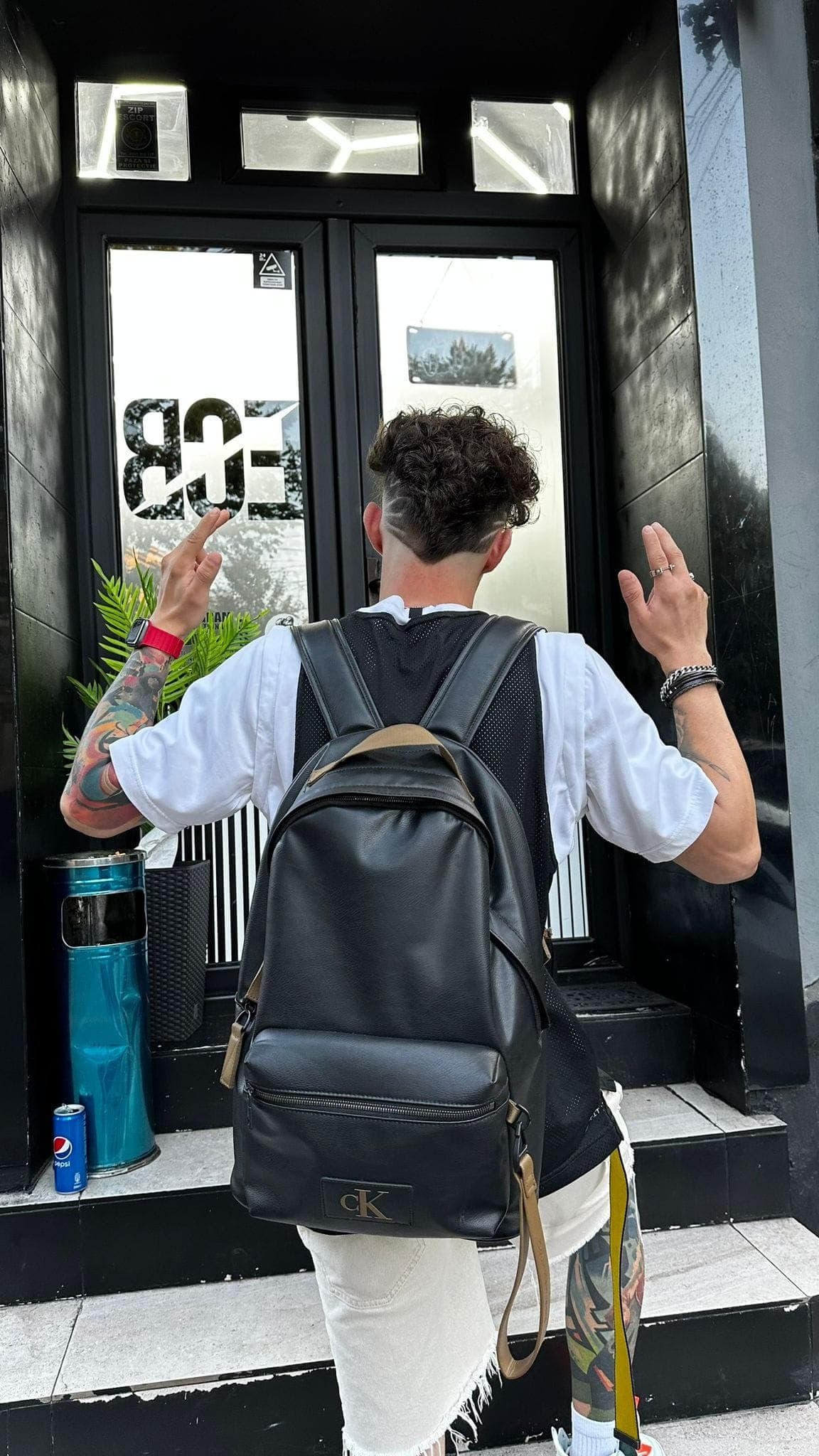 Tânăr cu rucsac Calvin Klein la ușa barbershop-ului cu logo ECB — client satisfăcut